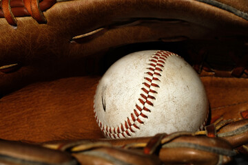 An old worn baseball sits inside a vintage leather baseball glove