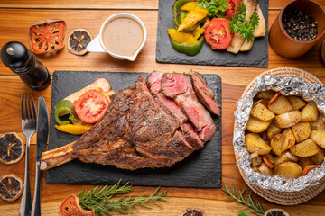 Grilled tomahawk ribeye steak in black stone plate on wooden table, Barbecue Tomahawk Steak on...