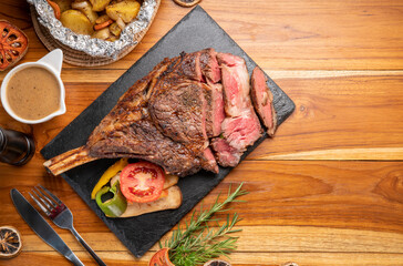 Grilled tomahawk ribeye steak in black stone plate on wooden table, Barbecue Tomahawk Steak on Cutting black stone plate.