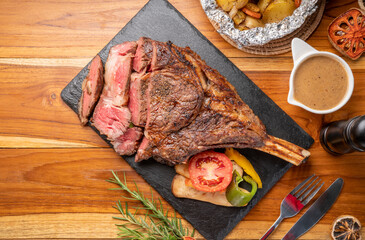 Grilled tomahawk ribeye steak in black stone plate on wooden table, Barbecue Tomahawk Steak on Cutting black stone plate.