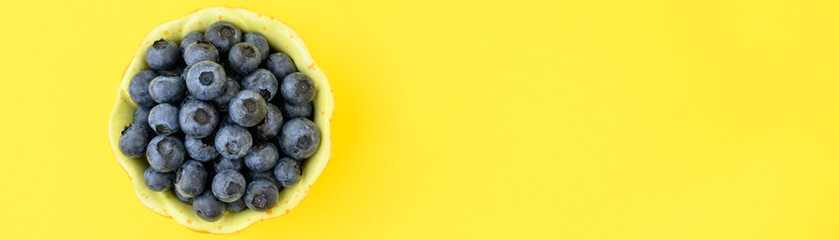 Fresh picked organic blueberries in a flower shaped bowl on a cheerful yellow background, tasty and nutritious
