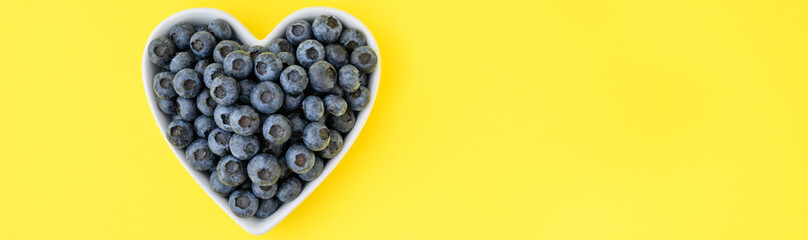 Fresh picked organic blueberries in a heart shaped bowl on a cheerful yellow background, tasty and...