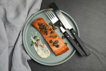 Delicious salmon with capers and sauce served on dark table, top view