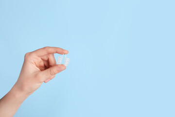 Woman holding anti-snoring device on light blue background, closeup. Space for text