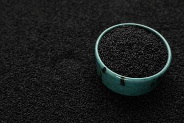 Bowl on pile of black sesame seeds, closeup. Space for text