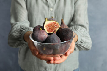 Woman holding glass bowl with tasty raw figs on light blue background, closeup