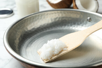 Frying pan with coconut oil and wooden spatula on white marble table, closeup. Healthy cooking