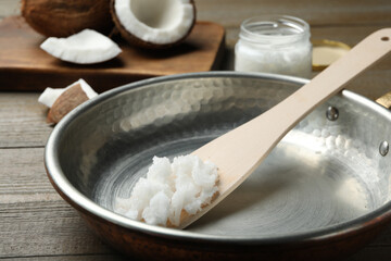 Fototapeta na wymiar Frying pan with coconut oil and wooden spatula on wooden table, closeup. Healthy cooking