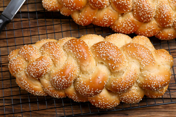Homemade braided breads with cooling rack on wooden table, flat lay. Traditional Shabbat challah