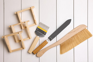 Honeycomb frames and beekeeping tools on white wooden table, flat lay