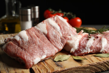 Raw ribs with bay leaves and pepper on wooden board, closeup