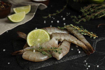 Fresh raw shrimps with lime and thyme on black table