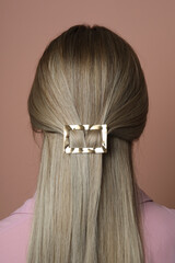 Young woman with beautiful gold hair clip pin on pink background, back view