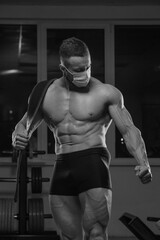Obraz na płótnie Canvas A medium long shot of a shirtless bodybuilder in a medical face mask who is posing after a workout. A muscular guy in a surgical mask is tensing his muscles in a gym.