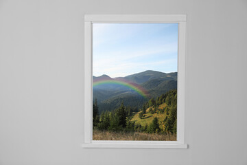 View of beautiful rainbow in mountains through window