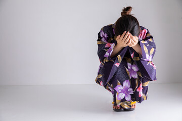 頭を抱えてしゃがみこむ浴衣の女性　Japan