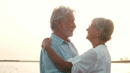 Close up of two cute and happy seniors having fun and enjoying together a sunset day at the beach. Mature couple in love kissing together with the sunset at the background.