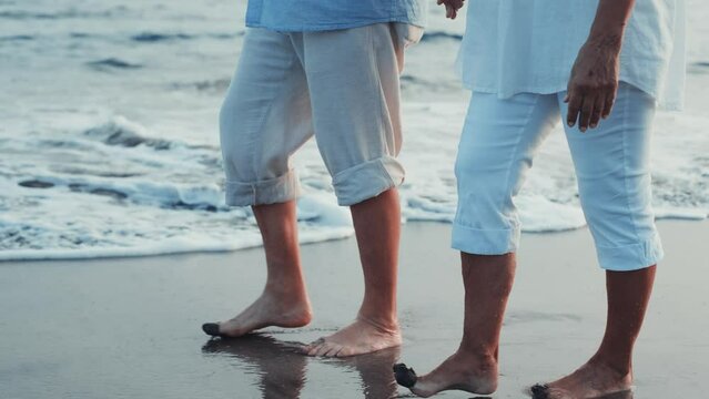Couple of old mature people walking on the sand together and having fun on the sand of the beach enjoying and living the moment. Two cute seniors in love having fun. Barefoot walking on the water
