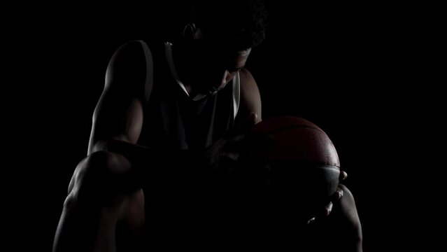 Basketball player sitting on a bench. Concentrated african american sports man against black background.