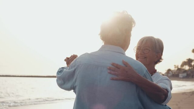 Couple of old mature people dancing together and having fun on the sand at the beach enjoying and living the moment. Portrait of seniors in love looking each others having fun.
