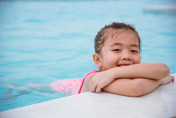 Toddler girl have fun swimming pool summer time with swimwear in blue water at hotel swimming pool outdoor. Kid swim playful water splash with happiness on summer vacation. Happy girl swim concept