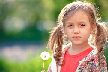 the little girl is  seriously looking at the camera and holding a glowing dandelion in her hand