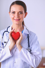 Beautiful young smiling female doctor sitting at the desk and holding heart.