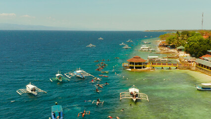 People snorkeling over coral reef with clear blue ocean water, top view. Moalboal, Philippines. People swim in the transparent sea between coral reefs. Summer and travel vacation concept.