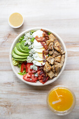 Healthy salad. Avocado, egg, chicken, tomato in a disposable bowl and orange juice in a disposable glass, on a wooden table