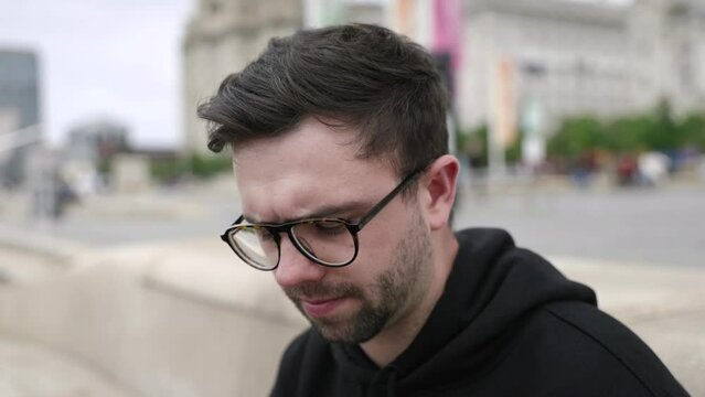 Young mid-twenties white male using mobile phone answering call in left hand looks to camera in cinematic slow motion. Tight shot showing Liverpool in background.