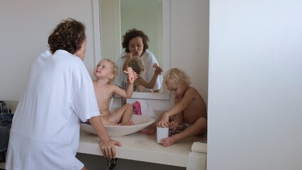 Mom with children in the bathroom brushes her teeth in the morning. The kid cleans his mother's teeth with a tooth tally with pleasure. Mom shows children how to brush their teeth.