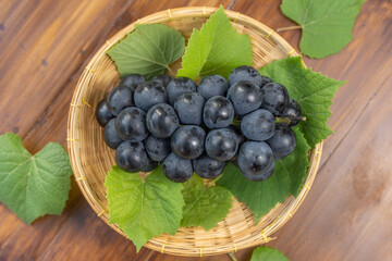 Black Grape on bamboo basket on wooden background, Kyoho Grape with leaves on wooden background.