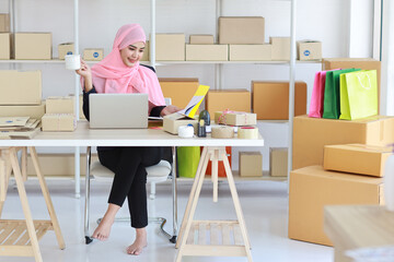 Active smiling asian woman in blue muslim suit sitting and working with online package box...