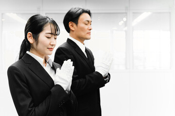 白手袋をつけて合掌するスーツ姿の男女（葬祭ディレクター・お葬式）
