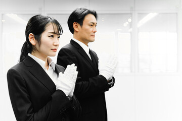 白手袋をつけて合掌するスーツ姿の男女（葬祭ディレクター・お葬式）
