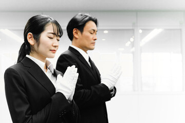 白手袋をつけて合掌するスーツ姿の男女（葬祭ディレクター・お葬式）
