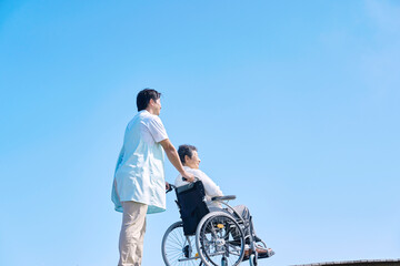 屋外で高齢者女性が乗る車椅子を押す介護士