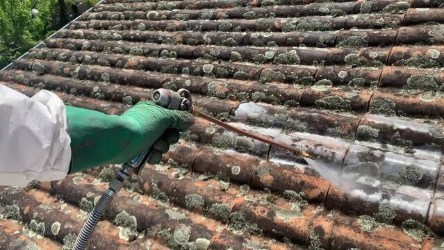 Worker's Hand In Glove Spraying Moss Remover On Roof Tiles With High Pressure Gun. close up