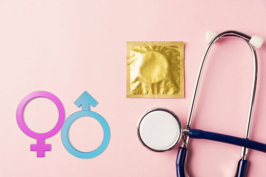 World sexual health or Aids day, Top view flat lay medical equipment, condom in pack, doctor stethoscope and Male and female gender signs, isolated on a pink background, Safe sex reproductive health