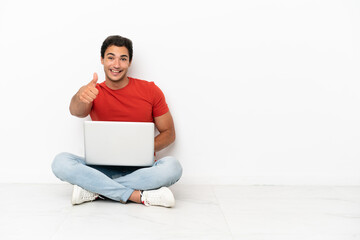 Caucasian handsome man with a laptop sitting on the floor with thumbs up because something good has happened