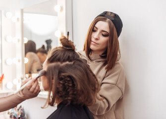Fototapeta premium Professional make-up and hair style artists doing make-up and hair curls to a beautiful caucasian woman in a beauty salon