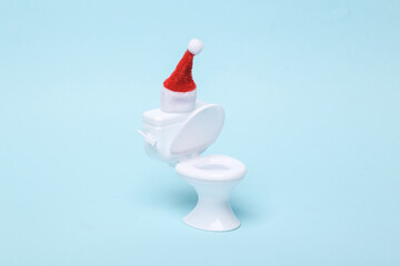 figurine of a mini toilet with a santa hat on a blue background. Merry Christmas. Minmal humor still life