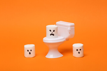 Minimal halloween still life. Toilet miniature with halloween marshmallows on orange background. Trick or treat.