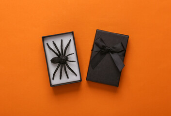 Black gift box with spider on orange background. Creative halloween layout. Top view. Flat lay