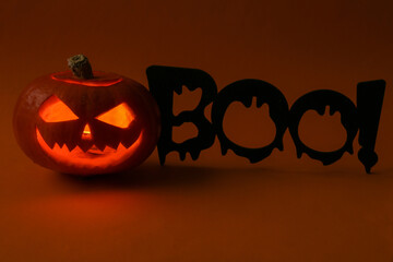 Halloween pumpkin head jack lantern with burning candles and word boo!on dark orange background