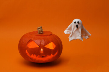 Halloween pumpkin head jack lantern with burning candles and ghost on orange background. Creative...