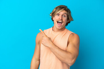 Handsome blonde man isolated on blue background surprised and pointing side