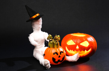 Halloween still life. Halloween pumpkin jack o lantern with mummy doll with candy bucket on black...