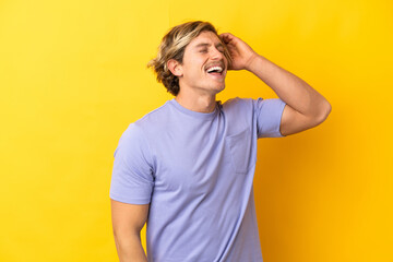 Handsome blonde man isolated on yellow background smiling a lot