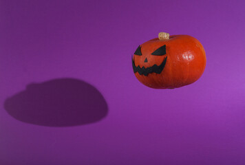 Floating halloween pumpkin with scary face on purple background with shadow